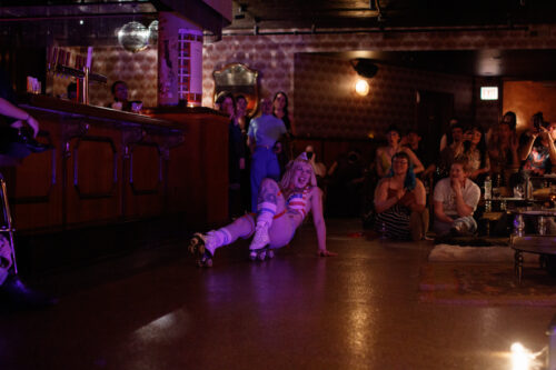 performer wearing roller skates does a move on the floor of the venue for the audience as they watch
